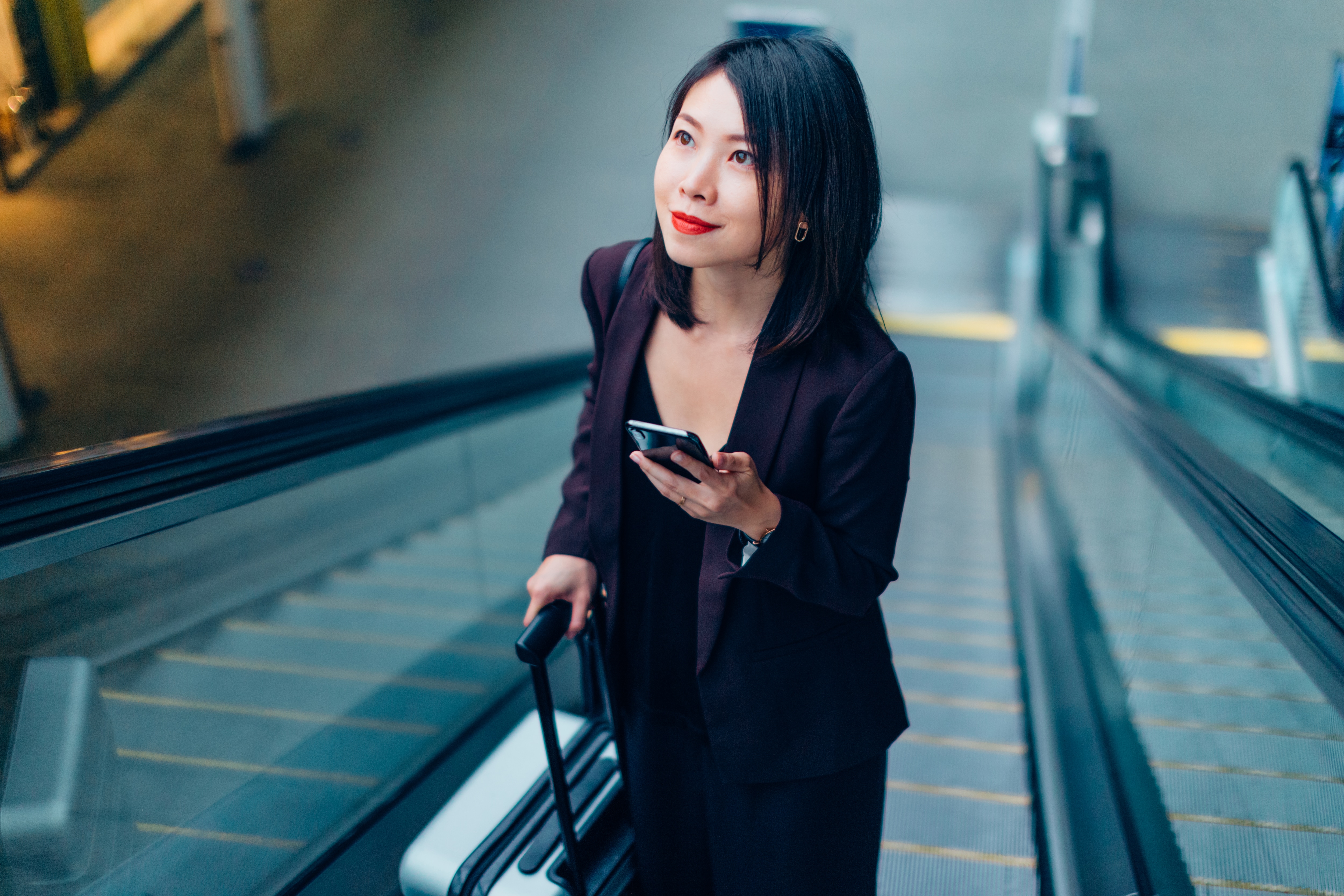 business traveler smiling on airport escalator as she embarks on a business trip