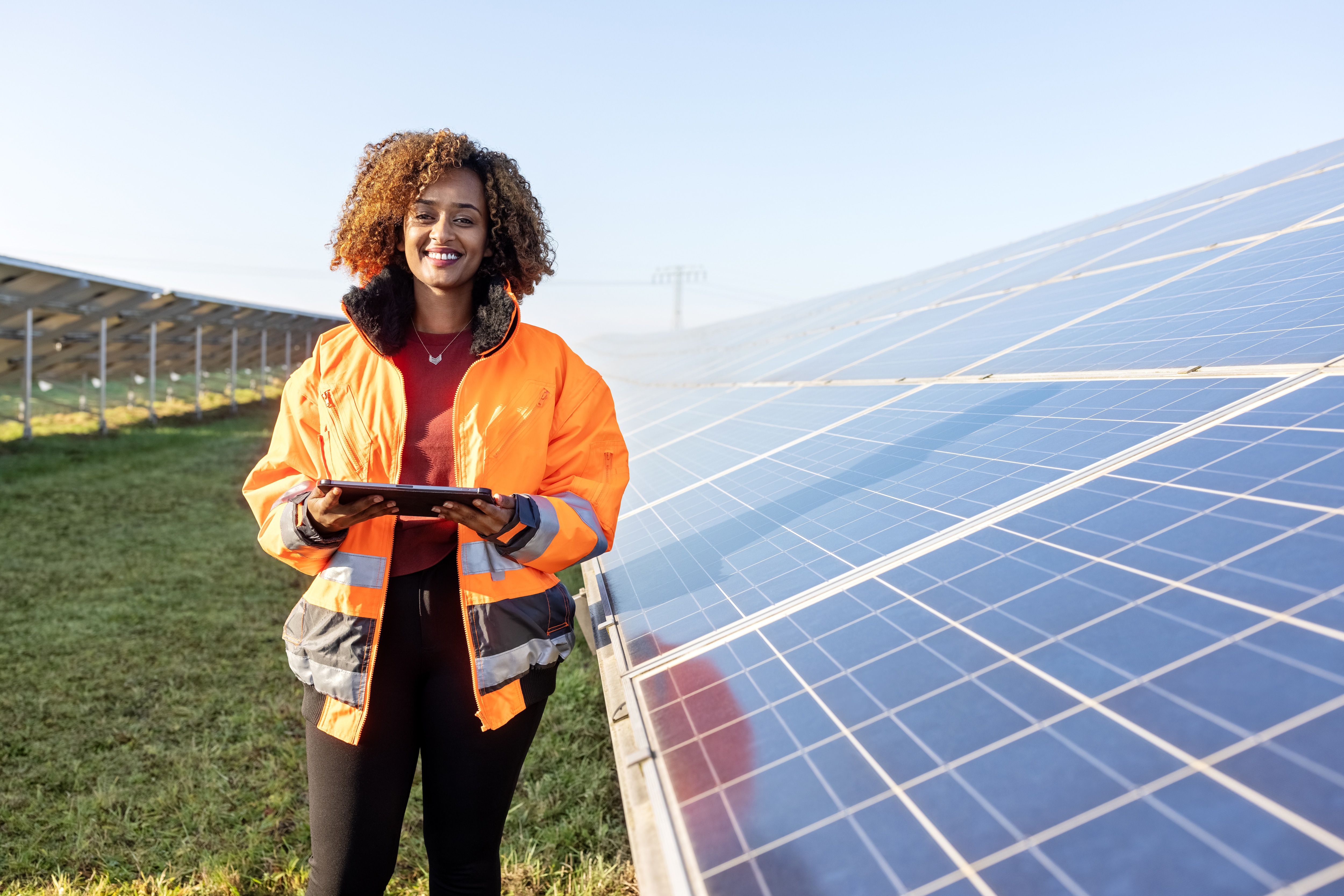 Lady standing in front of solar panels with an ipad, excited about T&E automation