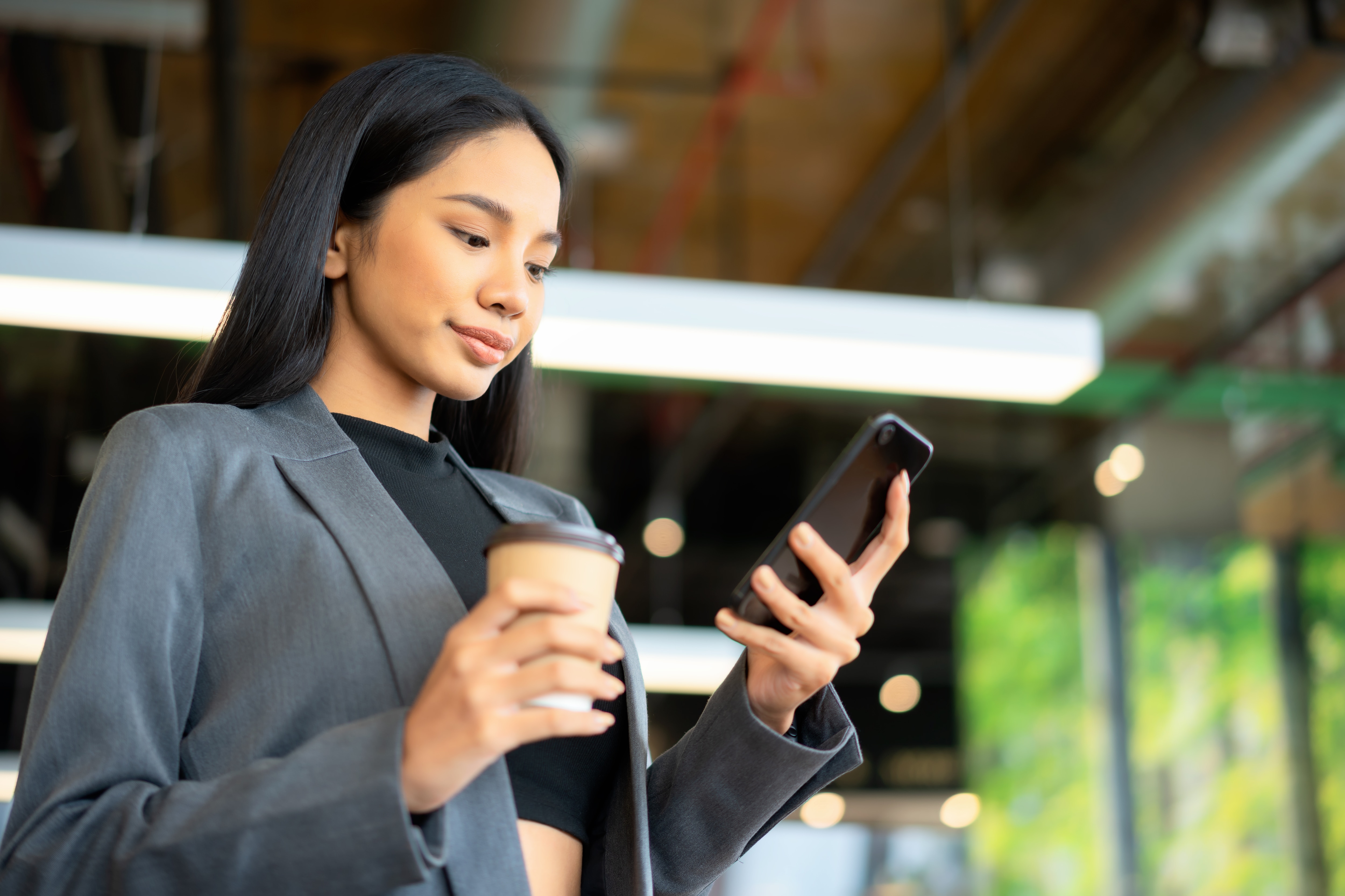 a woman holding a cup of drink and looking at her mobile device