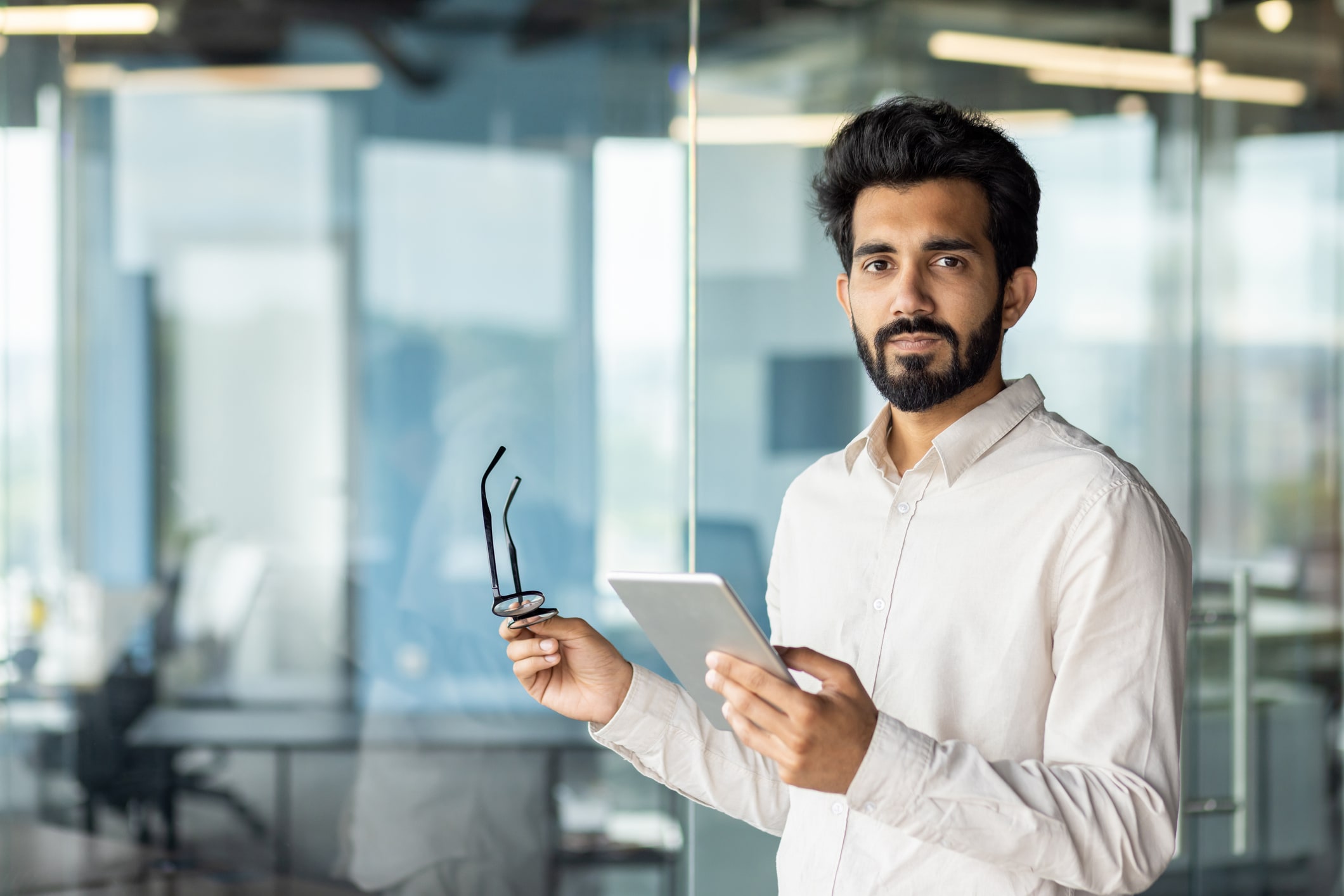 Man holding glasses in one hand and tablet in other